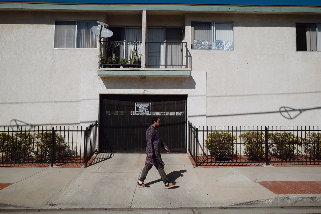 A side view of a person walking down a sidewalk next to an apartment building.
